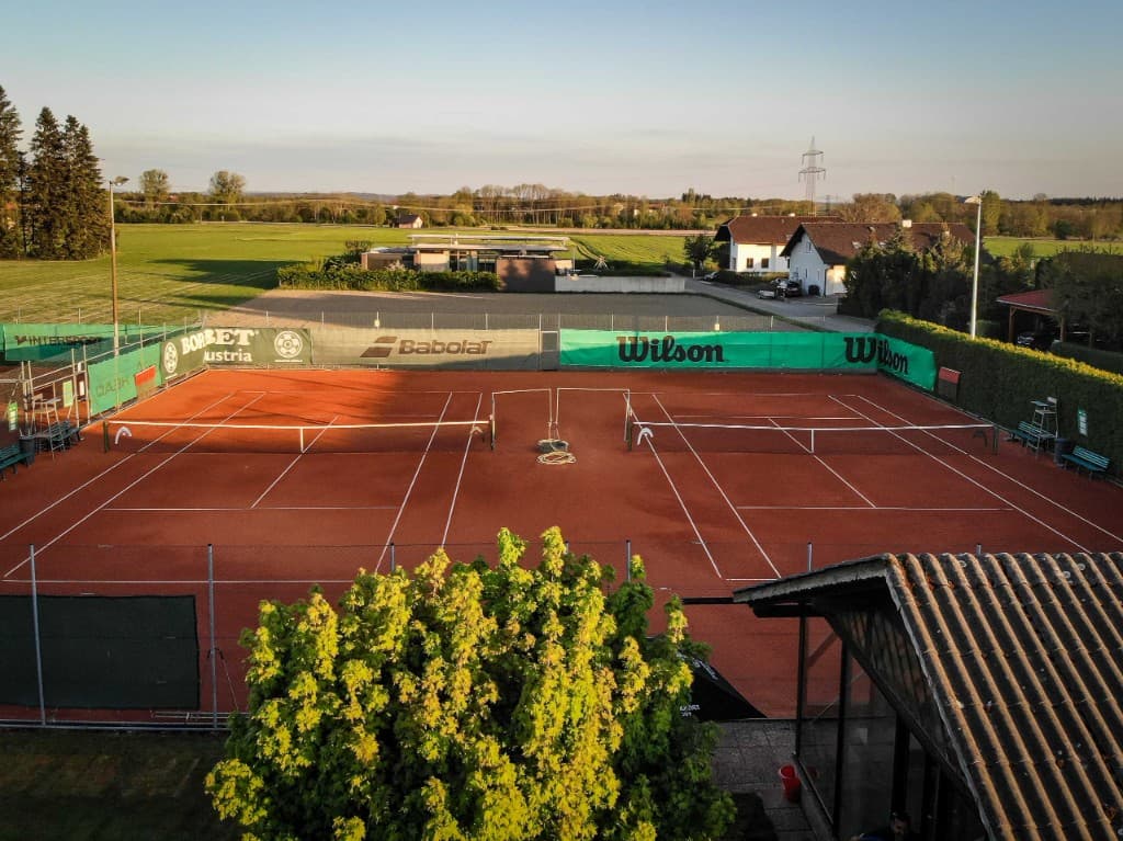 Two TC Mining clay courts in warm evening light, surrounded by sponsor banners and green fields